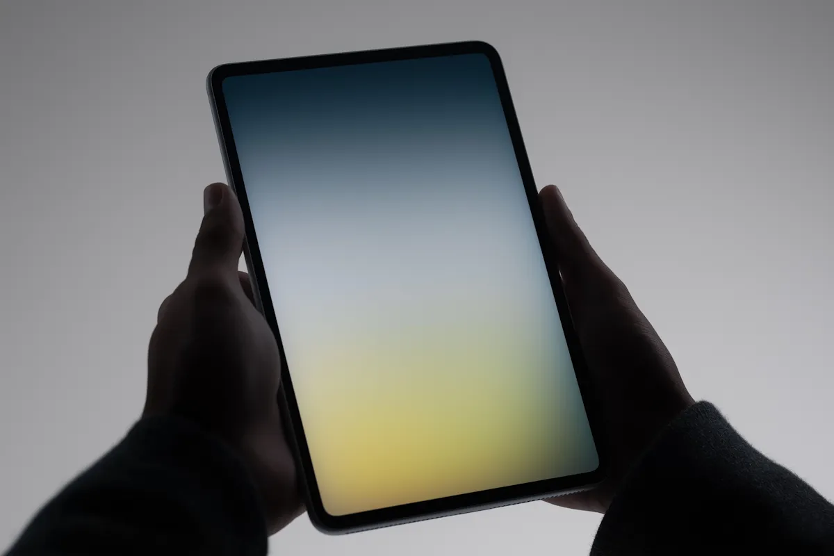 Silhouetted hands holding a tablet displaying a gradient screen fading from blue at the top to yellow at the bottom.